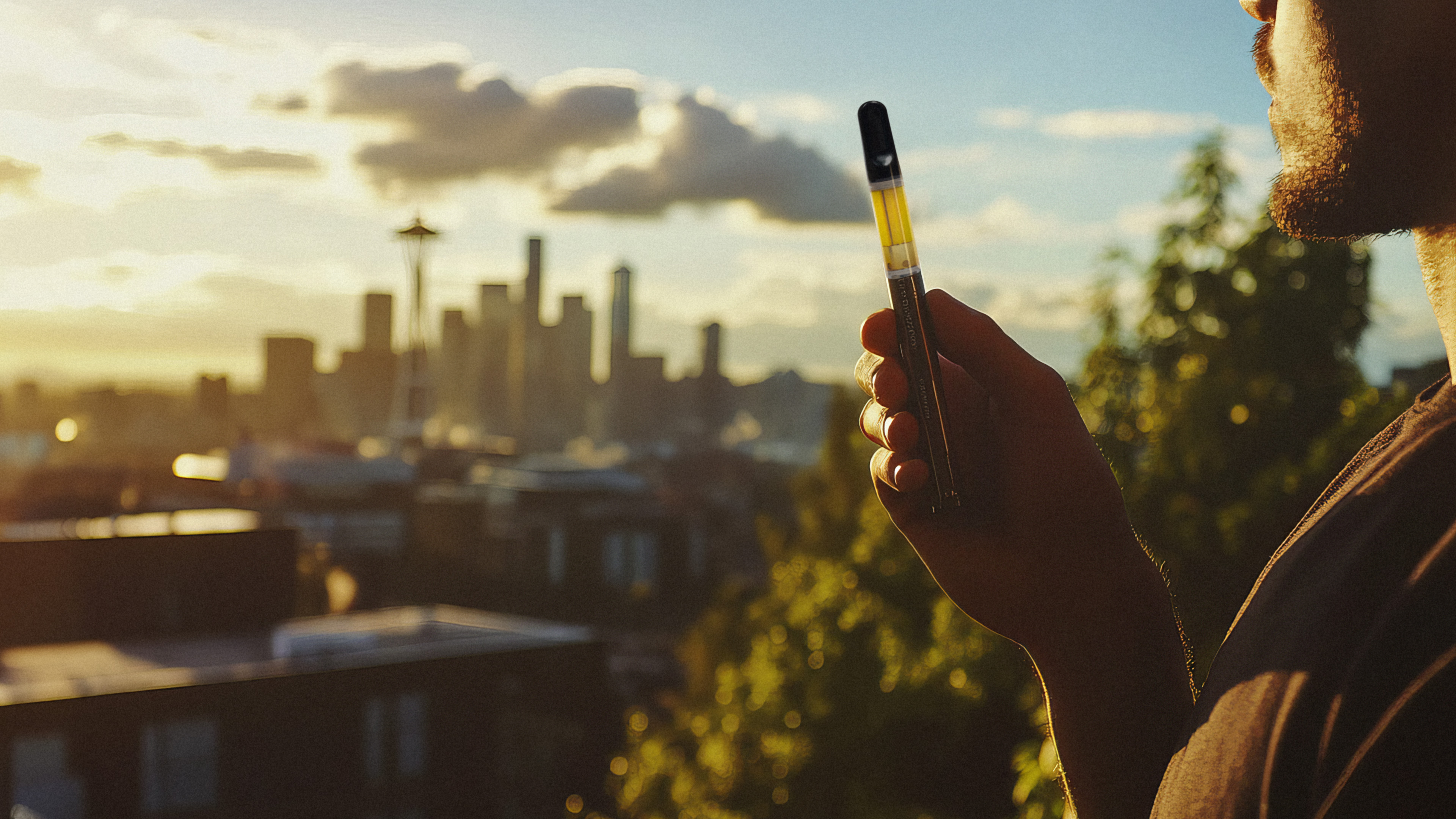 A hand holding a rechargeable vape unit in the woods.